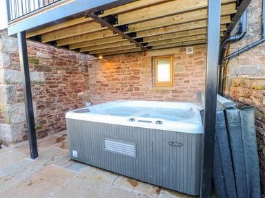 An outdoor hot tub under a wooden deck with stone walls at Apple Tree Cottage in Bleatarn near Kirkby Stephen