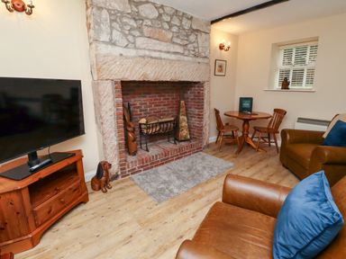 A living room with a stone and brick fireplace two brown leather armchairs a wooden round table with two chairs and a television on a wooden stand at Bracken Lodge in Wooler