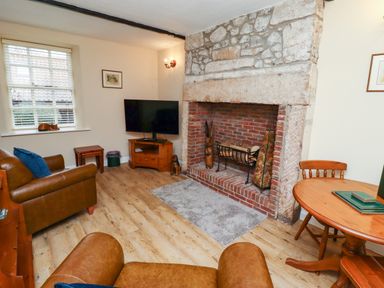 A living room with a stone fireplace a television two leather chairs and a round wooden table at Bracken Lodge in Wooler