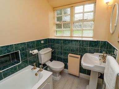 A bathroom with a bathtub toilet sink and window with blinds at Bracken Lodge in Wooler