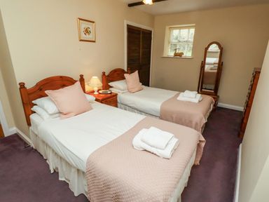 A bedroom with two single beds with white and pink bedding a bedside table with a lamp a standing mirror and a window at Bracken Lodge in Wooler