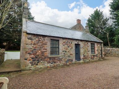 A stone cottage with a gray door and two windows surrounded by trees at Bracken Lodge in Wooler