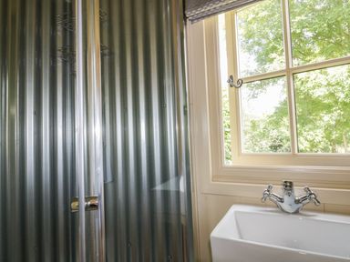 A metal shower enclosure next to a window with a sink and faucet at Orchard Burlawn near Wadebridge