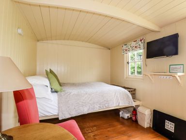 A small bedroom with a bed two green pillows a red chair a wall-mounted television and a window at Orchard Burlawn near Wadebridge