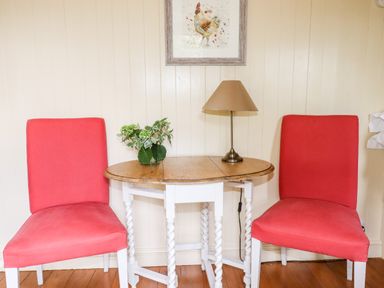 A small wooden table with a lamp and plant between two red chairs in a room at Orchard Burlawn near Wadebridge