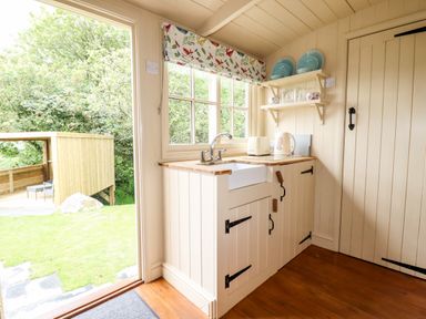 A small kitchen area with a sink toaster kettle and shelves with plates and cups at Orchard Burlawn near Wadebridge
