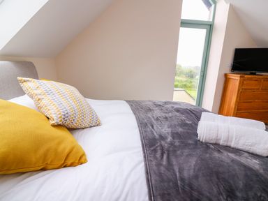 A bedroom with pillows on a bed towels on a blanket a wooden dresser with a television at Bwthyn Eisteddfa Fach in Brynberian near Newport