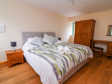 A bedroom with a bed a bedside table lamp a wooden wardrobe and a desk with a stool at Bwthyn Eisteddfa Fach in Brynberian near Newport