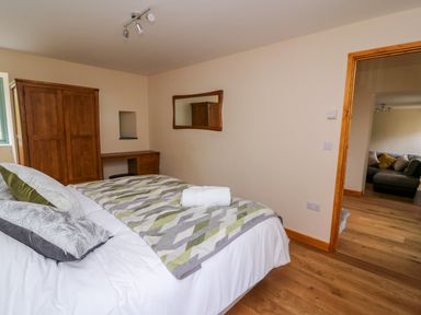 A bedroom with a bed covered in patterned blanket and pillows a wooden wardrobe a desk and a mirror on the wall at Bwthyn Eisteddfa Fach in Brynberian near Newport