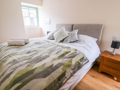 A bedroom with a bed with patterned blanket and pillows next to a window and wooden nightstand with lamp at Bwthyn Eisteddfa Fach Brynberian near Newport