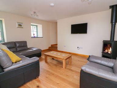A living room with grey leather sofas a wooden coffee table a wall-mounted television and a wood-burning stove at Bwthyn Eisteddfa Fach in Brynberian near Newport
