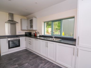 A kitchen with white cabinets a black countertop a stainless steel oven and hood a sink under a window at Bwthyn Eisteddfa Fach in Brynberian near Newport