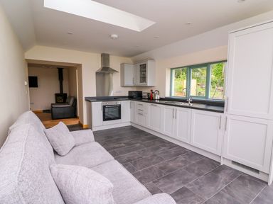 A kitchen with white cabinets a black countertop and a gray tiled floor next to a light gray sofa at Bwthyn Eisteddfa Fach in Brynberian near Newport