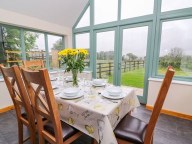 A dining area with a table set for six and yellow flowers in a glass vase by large windows at Bwthyn Eisteddfa Fach in Brynberian near Newport