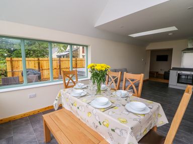 A dining area with wooden chairs and bench around a table set with white dishes and yellow flowers on a tablecloth at Bwthyn Eisteddfa Fach in Brynberian near Newport