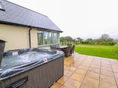 A patio with a hot tub and outdoor dining table overlooking a grassy yard at Bwthyn Eisteddfa Fach in Brynberian near Newport