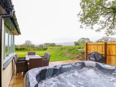 An outdoor patio with a hot tub a table with six chairs and a wooden fence at Bwthyn Eisteddfa Fach in Brynberian near Newport
