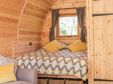A wooden bedroom with a bed with patterned bedding and yellow pillows and a window with curtains at Dingle Den in Craswall