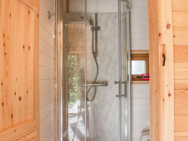 A shower with glass doors and a showerhead in a wooden bathroom at Dingle Den in Craswall