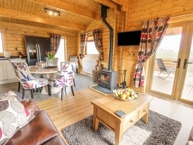 A living area with leather sofa, dining table with floral chairs, wood burner, and glass doors at Manor Farm Lodges - Red Kite Lodge in Newtown