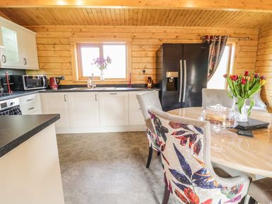 A kitchen with white cabinets a black refrigerator and a dining table with flowers at Manor Farm Lodges - Red Kite Lodge in Newtown