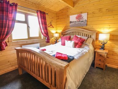 A bedroom with a wooden bed frame red plaid pillows and lamps at Manor Farm Lodges - Red Kite Lodge in Newtown