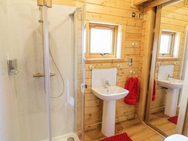 A bathroom with a shower enclosure a white sink with a red towel and a large mirror at Manor Farm Lodges - Red Kite Lodge in Newtown