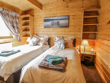 A bedroom with two single beds wooden walls and shelves a lamp and window at Manor Farm Lodges - Red Kite Lodge in Newtown