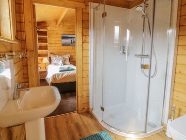 A bathroom with a shower cubicle and sink leading to a bedroom with a bed at Manor Farm Lodges - Red Kite Lodge in Newtown