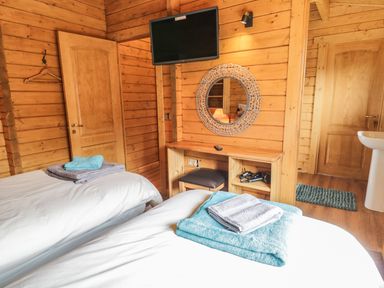 A bedroom with two beds a wall mounted tv a wooden desk and a round mirror at Manor Farm Lodges - Red Kite Lodge in Newtown