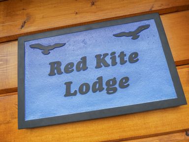A wooden wall with a blue sign that reads Red Kite Lodge with bird silhouettes at Manor Farm Lodges - Red Kite Lodge in Newtown