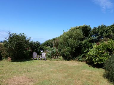A garden area with two plastic chairs on grass surrounded by bushes at The Quillet in Pendeen