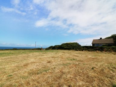 A field with dry grass and a house near the edge of the field with a view of the sea and sky at The Quillet in Pendeen