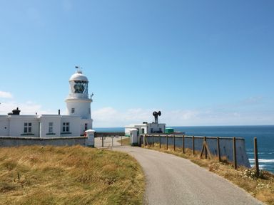 A lighthouse building near the coast beside a pathway with grass and a fence at The Quillet in Pendeen