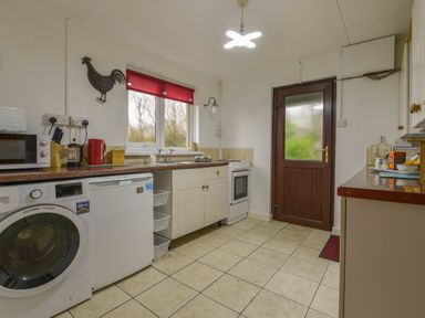 A kitchen with a washing machine microwave stove and red window blind at The Quillet in Pendeen