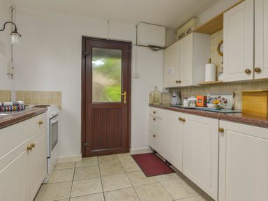 A kitchen with white cabinets and a wooden door with frosted glass at The Quillet in Pendeen