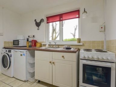A kitchen with a washing machine fridge microwave kettle stove and sink under a window at The Quillet in Pendeen