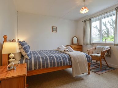 A bedroom with a bed a lamp bedside table a chair and a window at The Quillet in Pendeen