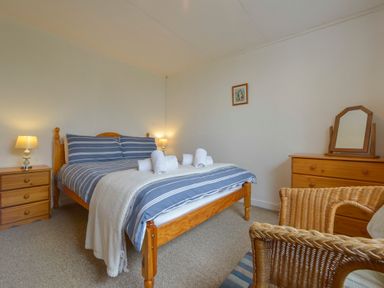 A bedroom with a wooden bed with striped bedding bedside tables with lamps a wooden dresser with a mirror and wicker chairs at The Quillet in Pendeen