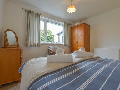 A bedroom with a bed covered in striped bedding and towels on top next to a wooden wardrobe and a dresser with mirror at The Quillet in Pendeen