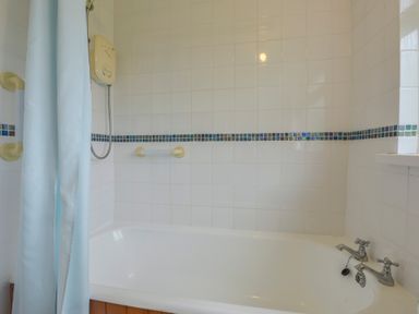 A bathtub with a shower and blue curtain in a tiled bathroom at The Quillet in Pendeen