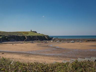 A beach with boats on sand and a grassy hill with a small building near the shore at Post House in Holsworthy