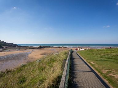 A paved path with a fence leading to a sandy beach with boats and the ocean at Post House in Holsworthy