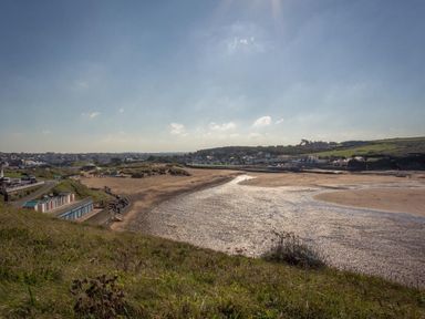 A coastal view with a sandy beach a path grassy hill and buildings in the distance at Post House in Holsworthy