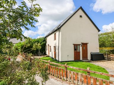 A detached two-story house with white walls and wooden doors surrounded by a green lawn and a wooden fence at Post House in Holsworthy