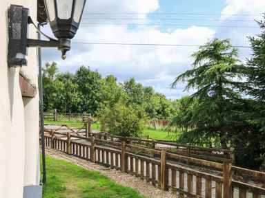 A wooden fence and gate along a gravel path with trees and grass in the background at Post House Holsworthy