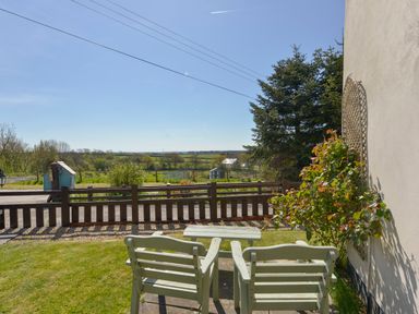 A garden area with two wooden chairs and a table facing a wooden fence and fields beyond at Post House in Holsworthy