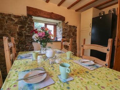 A dining table set with plates cups and a teapot in a kitchen with stone walls at Post House in Holsworthy