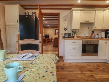 A kitchen with a dining table and chairs a black refrigerator white cabinets an oven and a toaster at Post House in Holsworthy