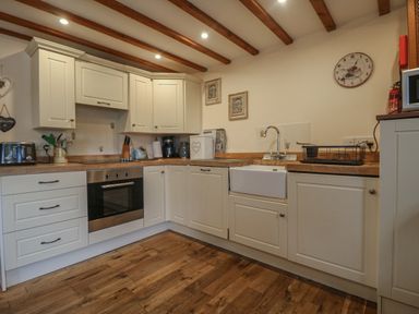 A kitchen with white cabinets wooden countertops a built in oven a farmhouse sink and a wooden floor at Post House in Holsworthy